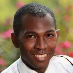 Headshot of Evander Baker.  A smiling black man in a white shirt with out-of-focus roses in the background.